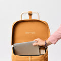 A female hand placing a laptop into the ochre Joyrolla Cart bag, with the lid lifted up for easy access. The image captures a close-up view of the hand holding a laptop and gently sliding it into the open bag. The vibrant ochre colour of the Joyrolla Cart bag stands out, adding a touch of style to the scene. This image demonstrates the versatility and functionality of the Joyrolla Cart, making it suitable for various uses, including carrying electronics securely.