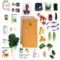 An overhead photo showcasing the spacious capacity of the Joyrolla Cart bag in Ochre. The bag is a flat lay, and it contains an assortment of fruit and vegetables, runners, and a magazine. The photo highlights the bag's large capacity, demonstrating its ability to accommodate a wide range of items, from groceries to personal belongings. With its generous space, the Joyrolla Cart bag provides ample room for carrying items, making it a versatile and practical choice for shopping, work, or everyday use.