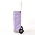 A side view of the lilac Joyrolla cart, highlighting its tall handle and sleek design. The cart features a long, ergonomic handle that reaches above waist height, allowing for comfortable maneuvering and effortless pushing or pulling. Its sleek design is characterized by clean lines and a streamlined silhouette. This lilac Granny cart combines functionality and style, offering a practical solution for transporting items with ease while exuding a modern aesthetic.