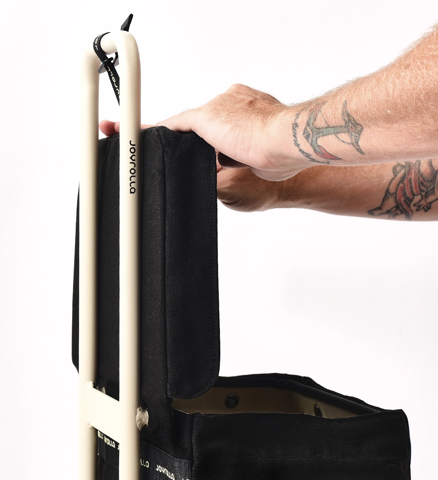 A close-up shot of the black Joyrolla Cart with a black bag attached. The frame of the cart is visible, showcasing its sturdy construction and sleek design. The lid of the cart is held up by a hand, revealing its easy-to-use functionality. The black bag attached to the cart adds storage capacity and is secured in place. This cart is a versatile and practical solution for transporting items with its durable frame, convenient lid, and ample storage space.